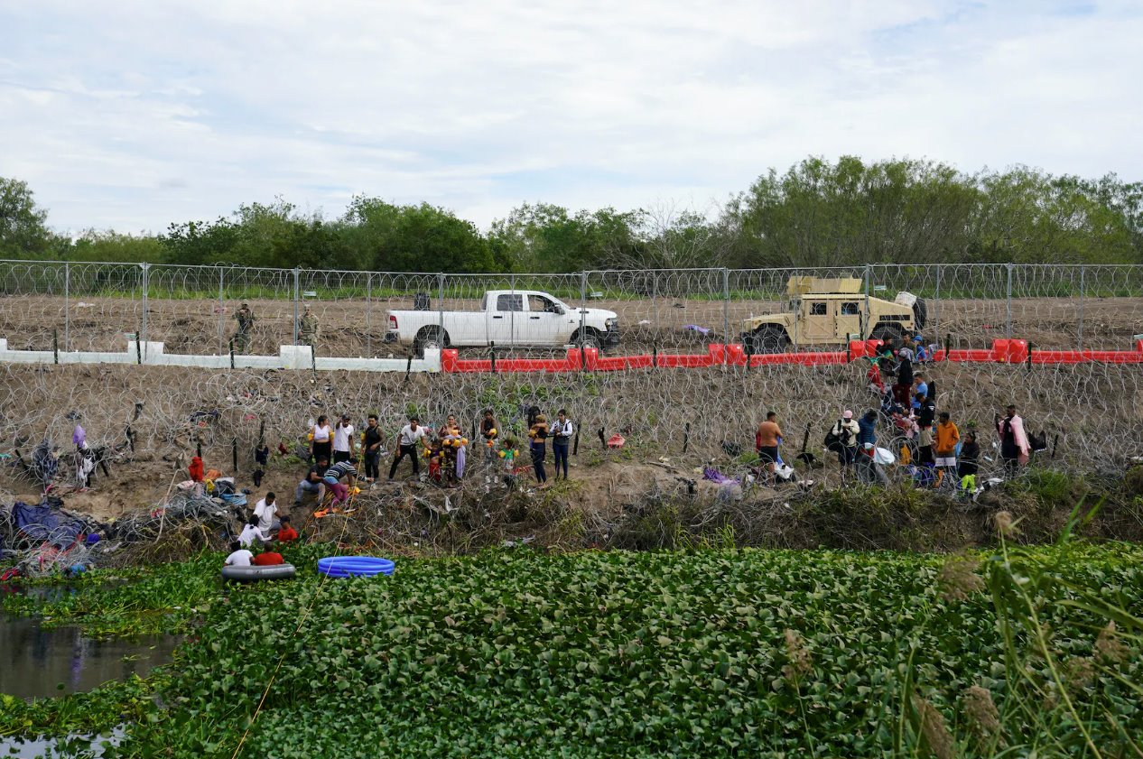 2023年12月29日，從墨西哥馬塔莫羅斯看到，人們在德克薩斯州布朗斯維爾的鐵絲網和新安裝的路障后面等待向美國邊境當局自首。