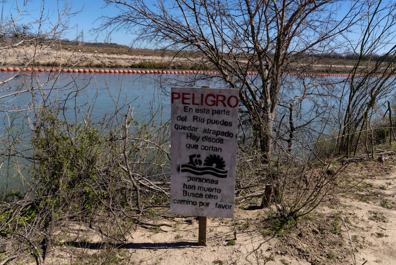 2024年2月25日,墨西哥科阿韋拉州彼德拉斯內格拉斯,一塊標志警告移民試圖通過格蘭德河上的漂浮屏障進入美國將面臨極大危險。