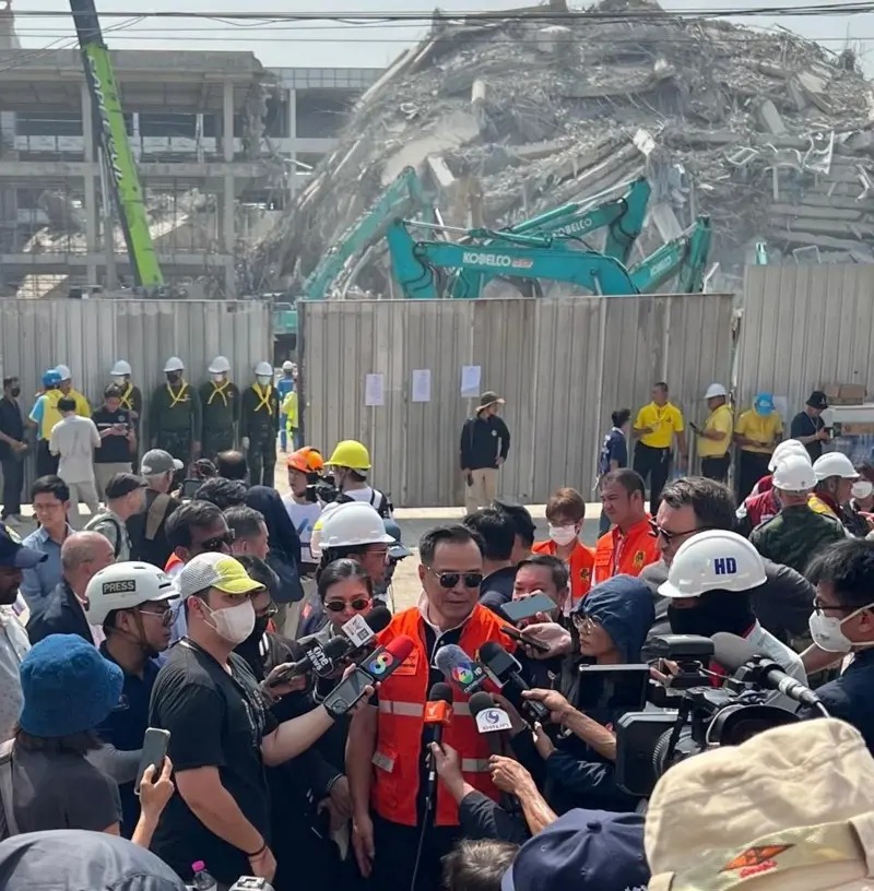 泰國副總理站在倒塌建筑的廢墟前，被記者包圍。